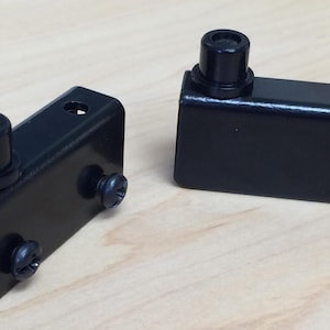 May include: Two black metal door hinges with a small black knob on each. The hinges are designed for glass doors.