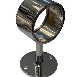 May include: A shiny, chrome-finished curtain rod bracket. The bracket has a circular ring to hold the rod, supported by a short, cylindrical post attached to a round base with screw holes. The metal reflects light.
