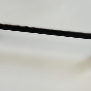May include: Black metal cabinet pull with a rectangular shape and a slightly curved design. The pull has a smooth, matte finish.