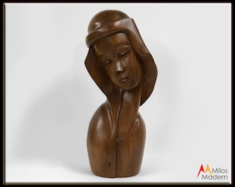 May include: A dark brown wooden sculpture of a woman's head and shoulders. The woman is wearing a head covering and has her eyes closed. The sculpture is carved in a stylized, abstract style.