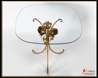 May include: A gold metal coffee table with a glass top and a floral design on the base.