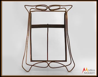 May include: A gold-toned metal picture frame with a simple, modern design. The frame has a rectangular shape with rounded corners and a decorative top.