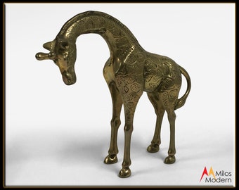 May include: A brass giraffe figurine with an elongated neck and detailed etched patterns. The giraffe is standing with its head lowered, showcasing the intricate design. The figurine is a decorative item, likely for display.