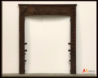 May include: A vintage cast iron fireplace mantel with intricate floral and scrollwork designs. The mantel is in a rusty brown color and has a rectangular opening for a fireplace.