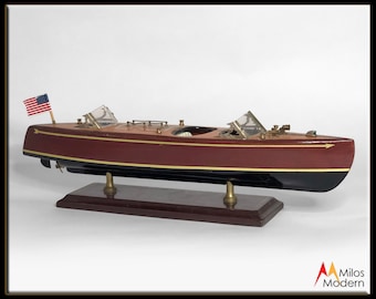 May include: A wooden model of a vintage mahogany speedboat with a black bottom, gold accents, and a small American flag on the bow. The boat is displayed on a wooden base.