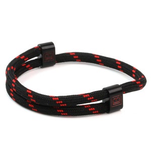 May include: Black and red rope bracelet with two metal clasps. The clasps have a small square logo.