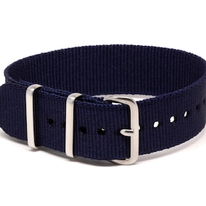 May include: A navy blue watch strap made of woven nylon fabric. The strap features a silver-colored buckle and two silver-colored loops. The strap has several holes for adjustment. The watch strap is designed to be durable and stylish.