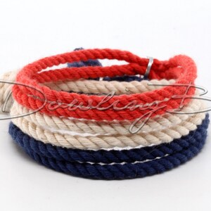 May include: A red, white, and blue rope bracelet with a silver clasp. The bracelet is made of three strands of rope, each a different color.