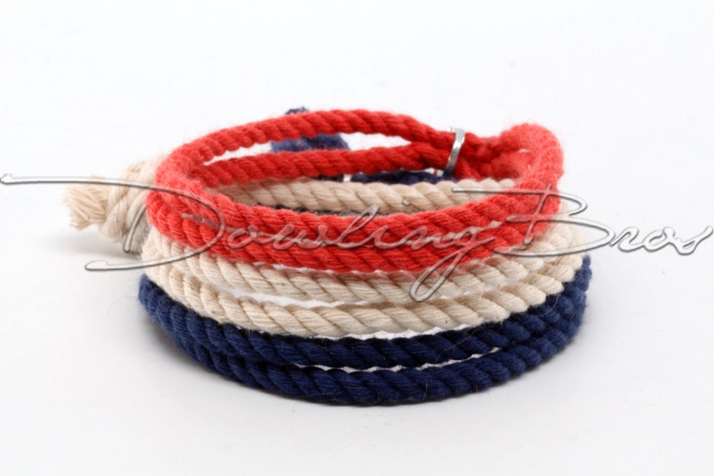 May include: A red, white, and blue rope bracelet with a silver clasp. The bracelet is made of three strands of rope, each a different color.