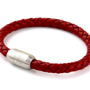 May include: A red leather bracelet with a silver magnetic clasp. The bracelet is braided and has a simple design.