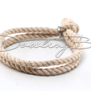 May include: A natural-colored rope bracelet with a metal ring closure. The rope is twisted and knotted to create a simple, yet stylish design.