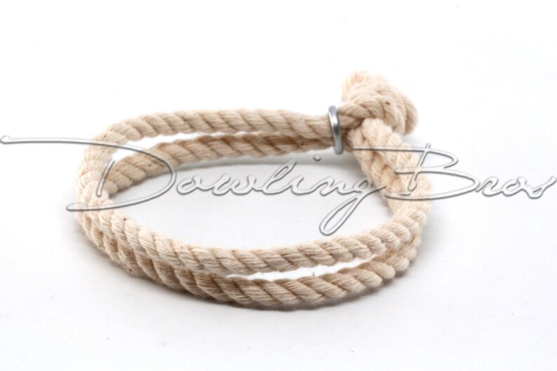 May include: A natural-colored rope bracelet with a metal ring closure. The rope is twisted and knotted to create a simple, yet stylish design.