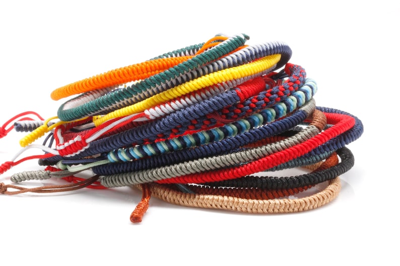May include: A stack of colorful braided bracelets in red, blue, green, yellow, orange, and white. The bracelets are made of woven string and are tied together in a knot.