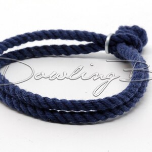 May include: A navy blue cotton rope bracelet with a silver metal clasp. The bracelet is tied in a knot at the end.