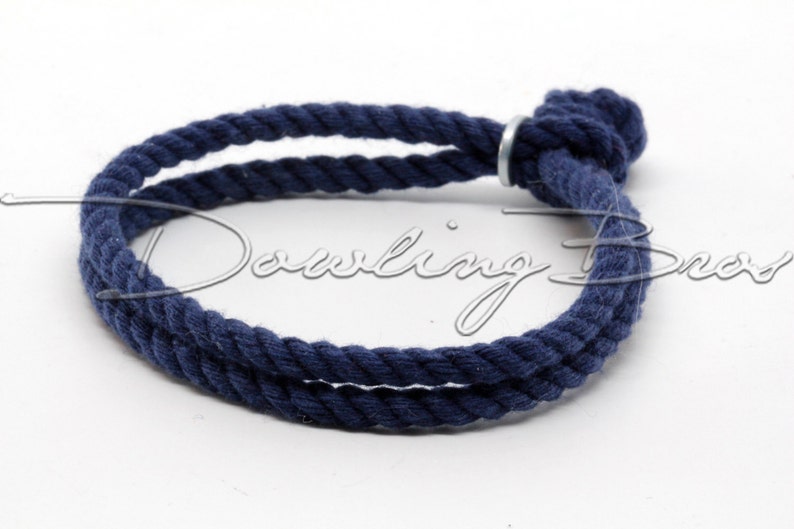 May include: A navy blue cotton rope bracelet with a silver metal clasp. The bracelet is tied in a knot at the end.