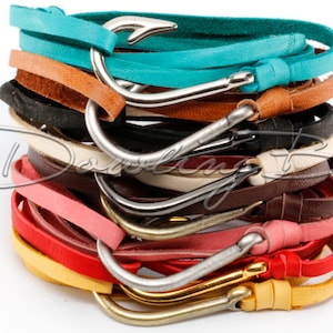 May include: A stack of colorful leather bracelets with silver hook clasps. The bracelets are in various colors, including turquoise, brown, black, cream, pink, red, and yellow.
