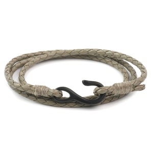 May include: A braided leather bracelet with a black hook clasp. The bracelet is a light brown color.