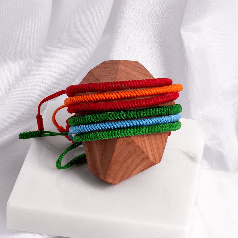 May include: A stack of colorful braided bracelets in red, orange, green, and blue, displayed on a wooden stand.