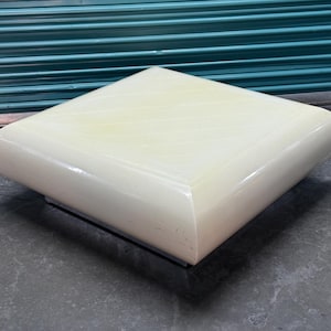 May include: A square, off-white coffee table with rounded corners. The table has a glossy finish and sits on a low, dark base. The design is modern and minimalist, suitable for living room decor.