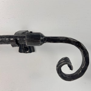 May include: Black metal curtain rod with a decorative scroll end. The rod is mounted to a white wall.