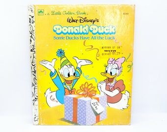May include: A yellow Little Golden Book featuring Donald Duck and Daisy Duck. The cover shows Donald Duck wearing a party hat and holding a gift box with a blue and white pattern. The gift box has a tag that says "For Daisy". The book title is "Some Ducks Have All the Luck".