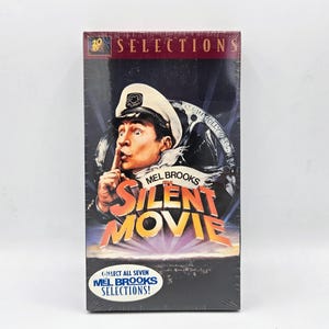 May include: A VHS tape case featuring Mel Brooks's "The Silent Movie". The cover art shows Mel Brooks in a captain's hat, with his finger to his lips, and the title in large, yellow letters. The text "Collect all seven Mel Brooks Selections!" is at the bottom of the case.