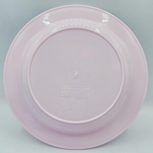 Puede incluir: Un plato de pl&aacute;stico rosa claro con un borde ligeramente elevado. El plato tiene una superficie lisa y un dise&ntilde;o circular. La parte inferior del plato tiene un peque&ntilde;o centro elevado con texto y s&iacute;mbolos en relieve.