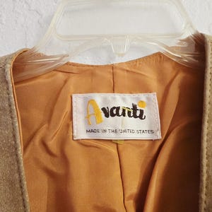 May include: Close-up of a tan suede vest with a gold satin lining. The vest is hanging on a clear plastic hanger. A label inside the vest reads "Avanti" and "Made in the United States".
