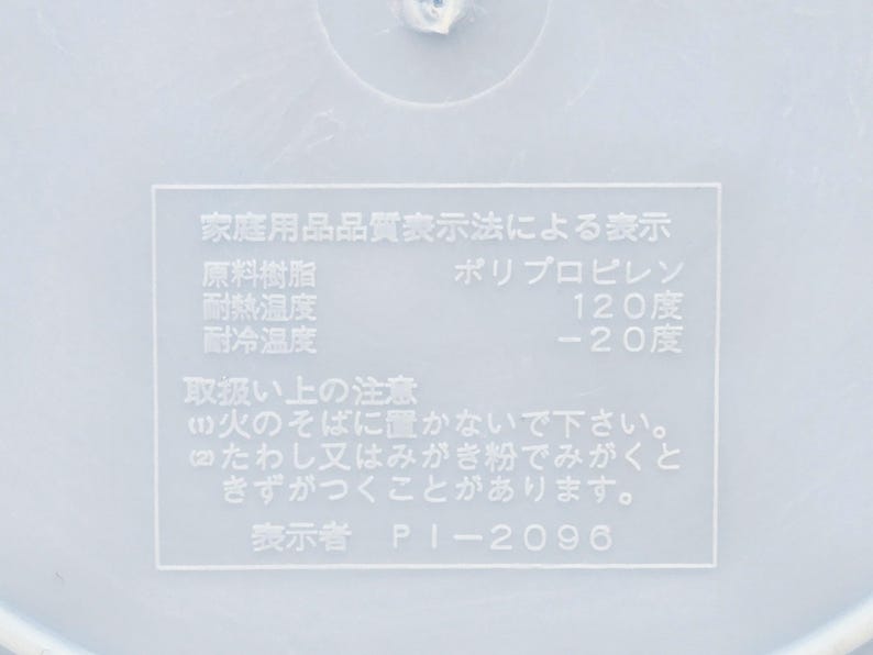 Puede incluir: Primer plano de una superficie de pl&aacute;stico blanco con texto japon&eacute;s. El texto incluye informaci&oacute;n sobre el material del producto, la resistencia al calor y al fr&iacute;o. El texto tambi&eacute;n incluye advertencias de uso.