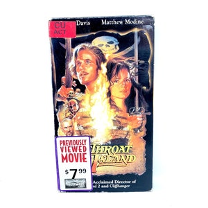 Puede incluir: Una cinta VHS de la película "Throat Island" protagonizada por Matthew Modine y con una etiqueta de precio roja de 7,99 $. La película se describe como una película vista anteriormente. El cartel de la película presenta un barco pirata y una calavera con huesos cruzados.