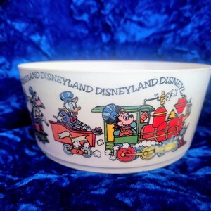 Puede incluir: Tazón de cerámica blanco con una ilustración colorida de Mickey Mouse, Donald Duck y Goofy montando un tren. El tazón tiene el texto "Disneyland Disneyland Disneyland" alrededor del borde.