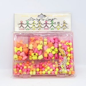 May include: A pink plastic container filled with colorful plastic beads and string for making jewelry. The container has the words "Make Your Own Jewelry String-a-Long" on the lid.