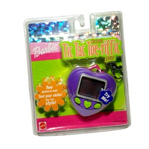 May include: A purple heart-shaped electronic game with a screen and buttons. The game is called "Barbie Tic Tac Toe-rific" and has a keychain attached. The packaging is pink, green, and orange with the text "Two games in one! Test your skills! Go for style!"