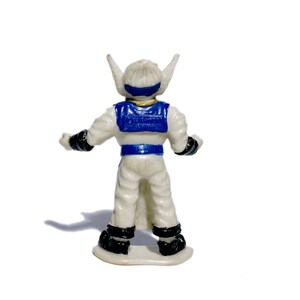 Puede incluir: Una figura de acci&oacute;n de pl&aacute;stico blanco con detalles azules y dorados. La figura tiene un casco blanco con una visera azul y una pieza de pecho azul y dorada. La figura est&aacute; de pie sobre una base blanca.