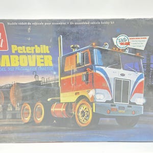 May include: An AMT Peterbilt Cabover Model 352 Pacemaker tractor hobby kit box. The box features a graphic of a red, white, and blue truck with yellow wheels. Text on the box includes amt, Peterbilt CABOVER, and Retro Deluxe Edition.