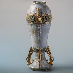 May include: A blue and gold ceramic vase with a decorative design. The vase has a wide mouth and a narrow base with three legs.
