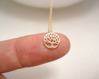 May include: A gold-toned necklace with a delicate tree of life pendant. The pendant is small and circular, with a detailed design of branches and leaves.