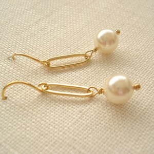 May include: A pair of gold earrings with a simple oval link and a white pearl dangling from each.