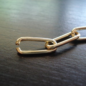 May include: A gold chain with a broken link. The chain is lying on a dark surface.