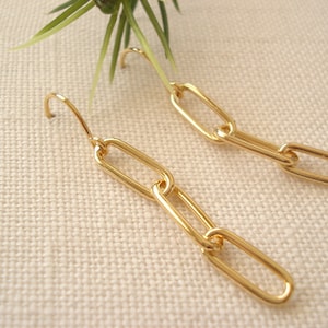 May include: Gold chain link earrings with a hook closure. The earrings are made of multiple connected oval-shaped links.