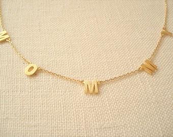 Puede incluir: Un collar de oro con las letras "MOM" escritas en una fuente simple y moderna.