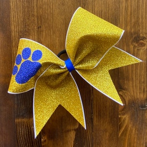 May include: Gold glitter cheer bow with a blue paw print and white trim.