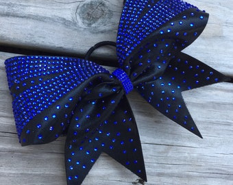 Puede incluir: Lazo de animadora negro y azul con brillantes pedrería azul. El lazo está hecho de tela negra con pedrería azul y un centro de pedrería azul. Se adjunta a una banda elástica negra.