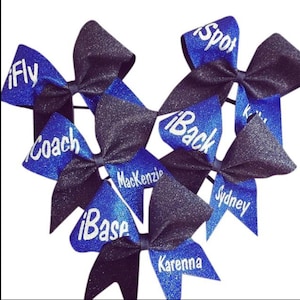 Könnte beinhalten: Ein Set aus sechs blauen und schwarzen Cheer-Schleifen mit weißen Glitzerbuchstaben. Die Schleifen sind mit den Worten "Fly", "Coach", "Base", "Back", "Spot" und "Mackenzie" verziert.