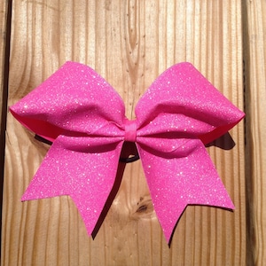 May include: A large pink glitter cheer bow with a black elastic band.