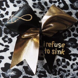 May include: A black and gold cheer bow with the text "I refuse to sink" on one side and an infinity symbol on the other side.
