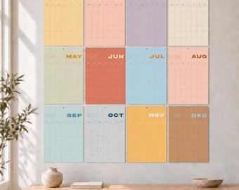 Puede incluir: Un conjunto de calendario de pared que consta de doce hojas rectangulares, cada una representando un mes de enero a diciembre. Cada hoja presenta un diseño de cuadrícula, un indicador numérico del mes y un fondo de color pastel o apagado distinto.