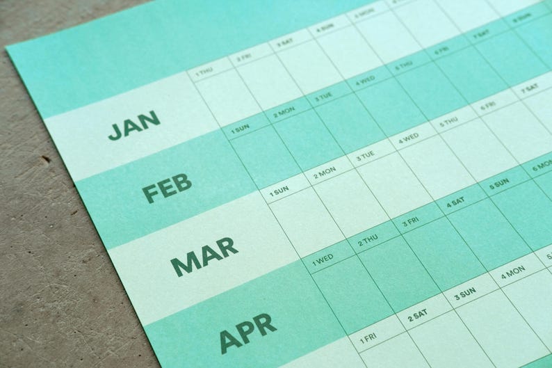 May include: A close-up of a teal and white yearly calendar. The months of January, February, March, and April are visible. The days of the week are listed across the top, with dates in the boxes below.