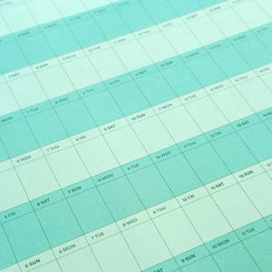 May include: A close-up of a teal and white weekly planner. The calendar grid features days of the week and dates, with a light teal background and white text. The layout is designed for detailed scheduling and organization.