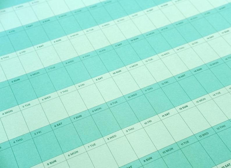May include: A close-up of a teal and white weekly planner. The calendar grid features days of the week and dates, with a light teal background and white text. The layout is designed for detailed scheduling and organization.